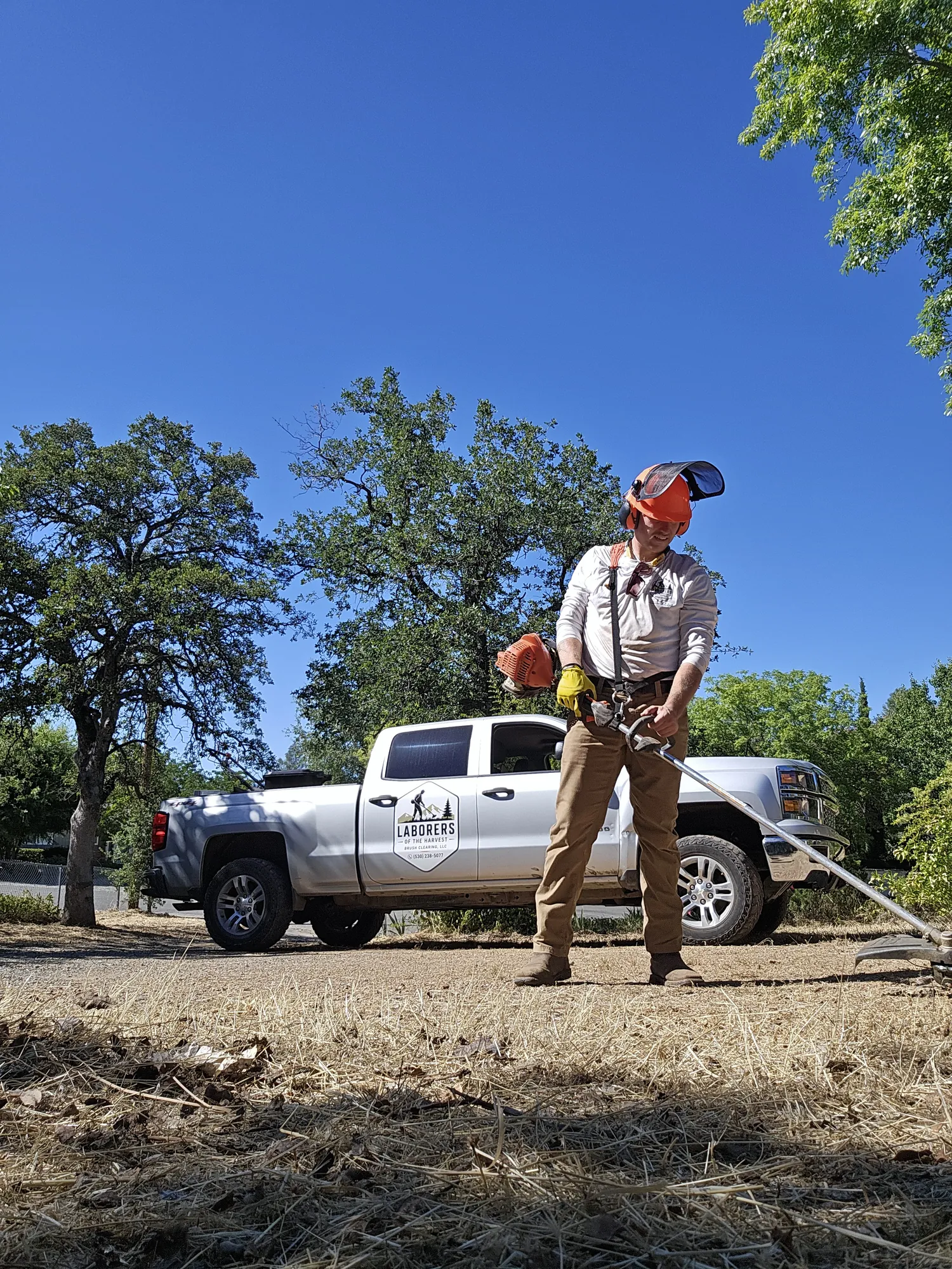 Crew member cutting brush beside the Laborers of the Harvest truck